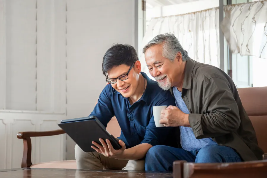 Older man holding a cup of coffee with younger man on couch
